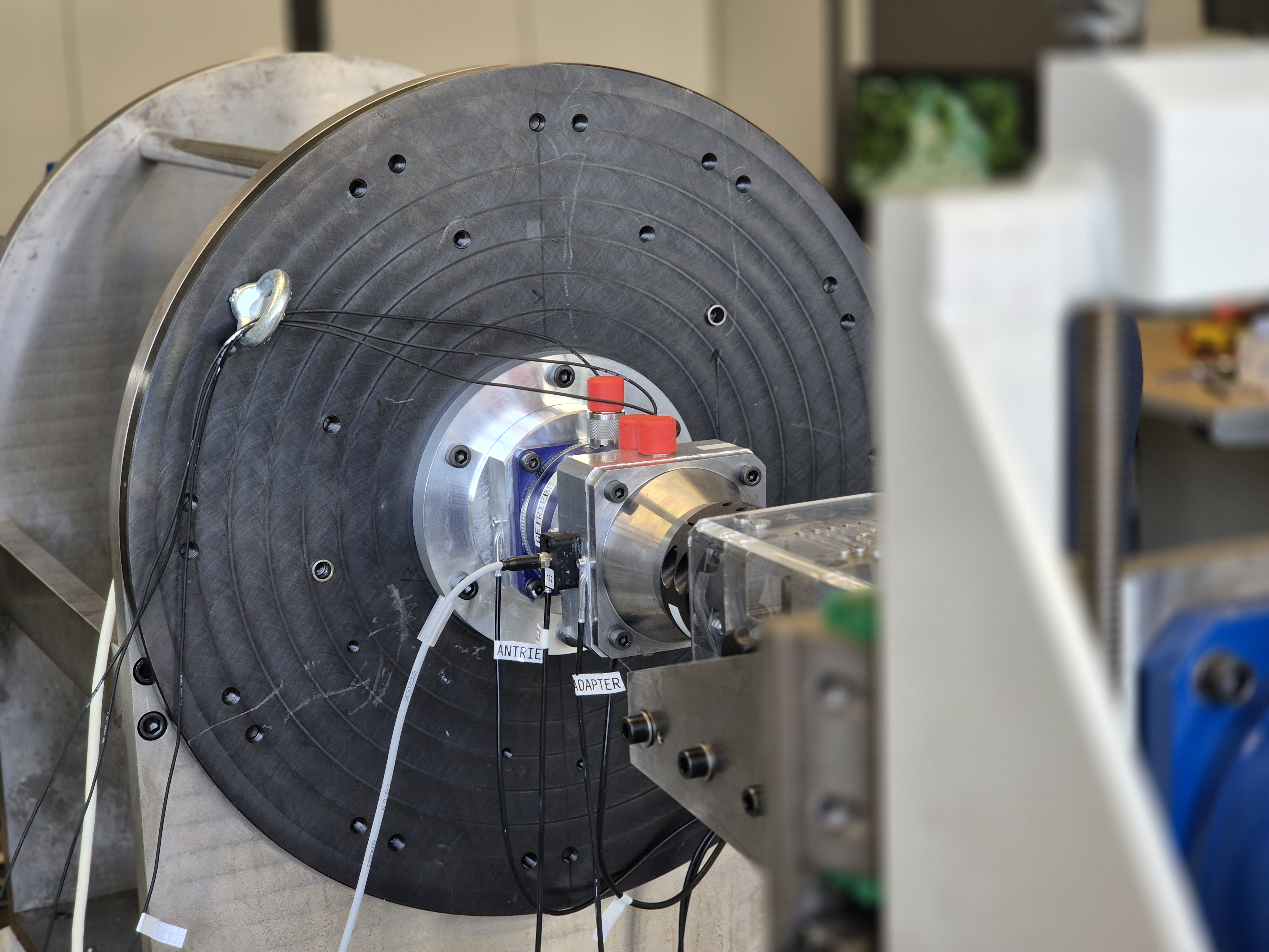 Blick auf einen Prüfstand mit einem montierten Planetengetriebe. An der Außenseite des Prüfgetriebes sind mehrere Sensoren verschiedener Bauart angebracht und mit Kabeln angeschlossen.