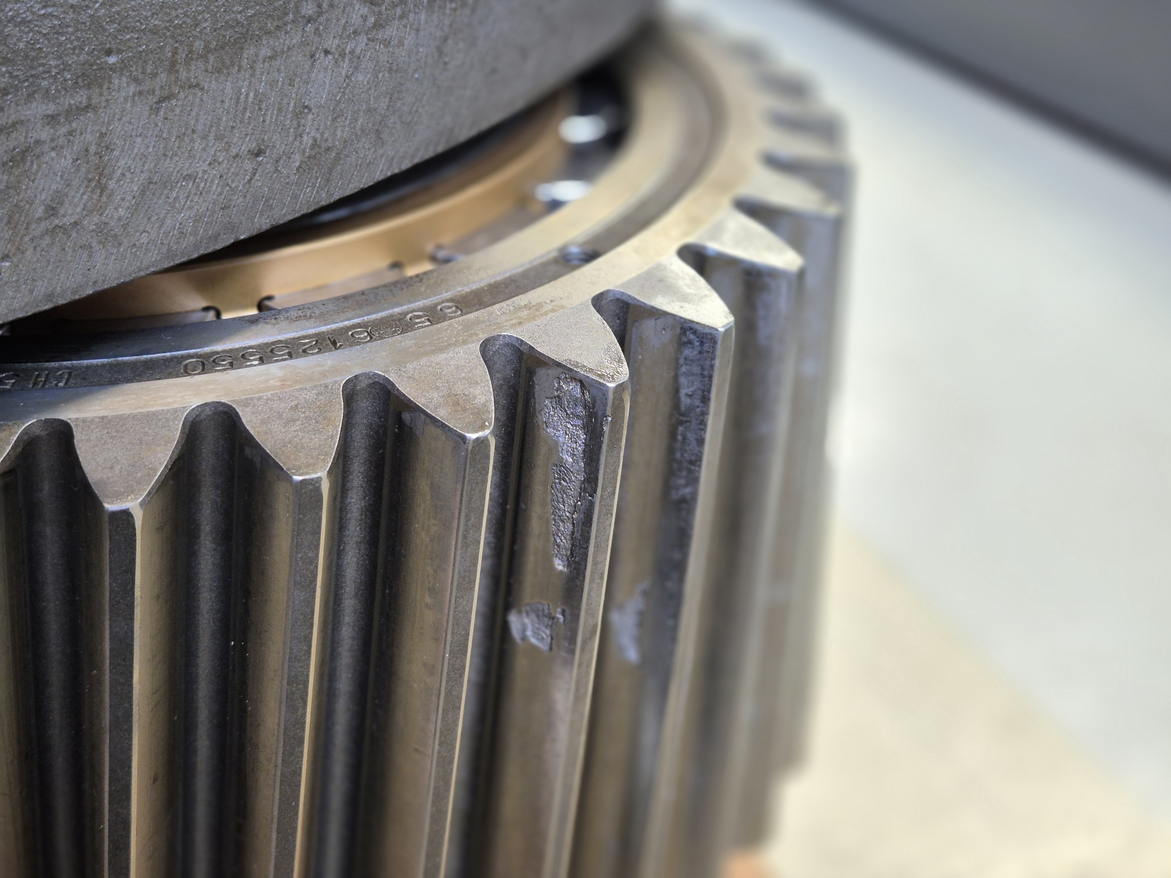 Nahaufnahme eines Zahnrads. Auf einer Zahnflanke ist ein Grübchenschaden sichtbar, der ca. ein Drittel der Zahnflankenfläche einnimmt.