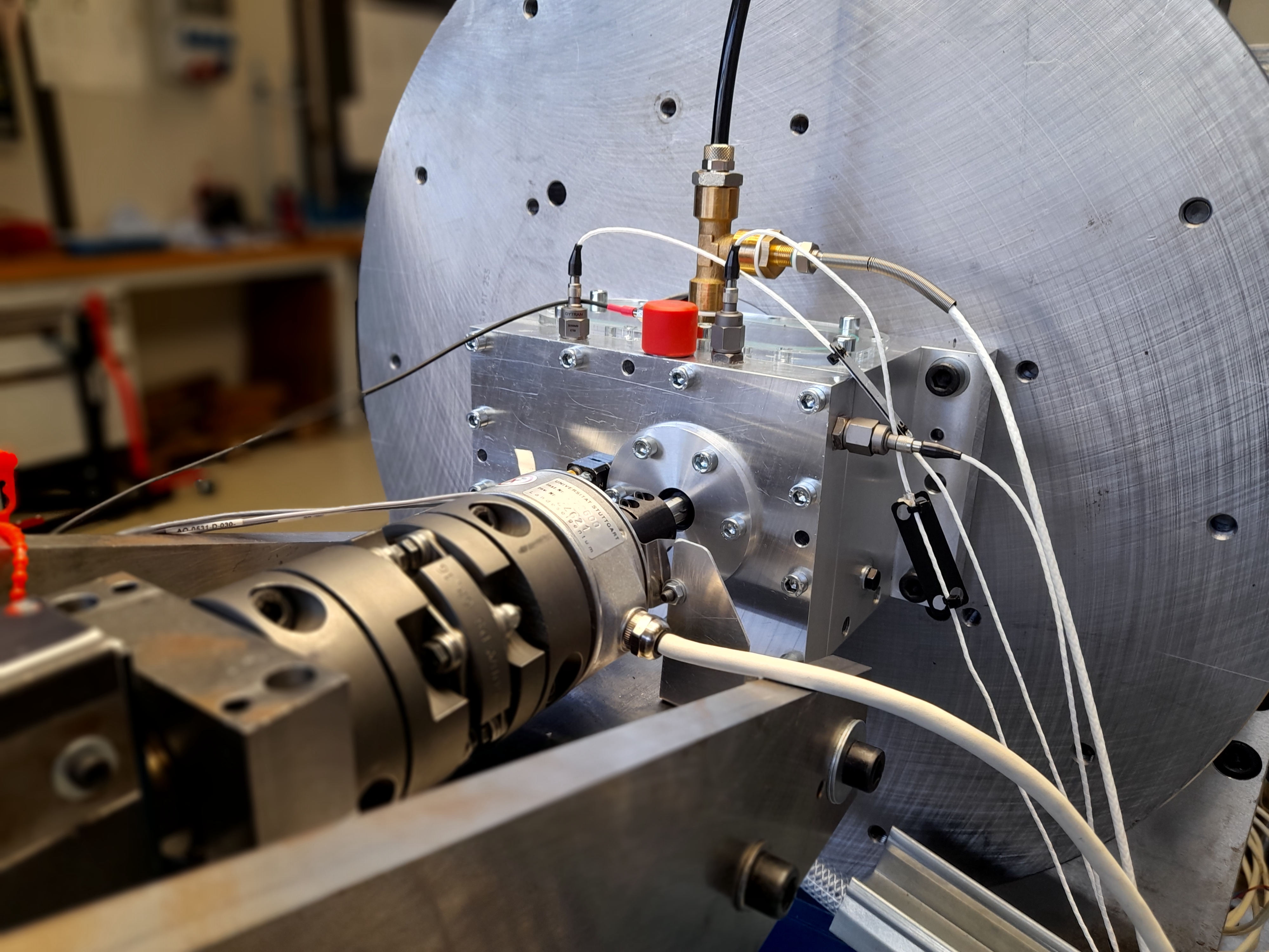 Blick auf einen Prüfstand mit einem montierten Prüfgetriebe. An der Außenseite des Prüfgetriebes sind mehrere Sensoren verschiedener Bauart angebracht und mit Kabeln angeschlossen.