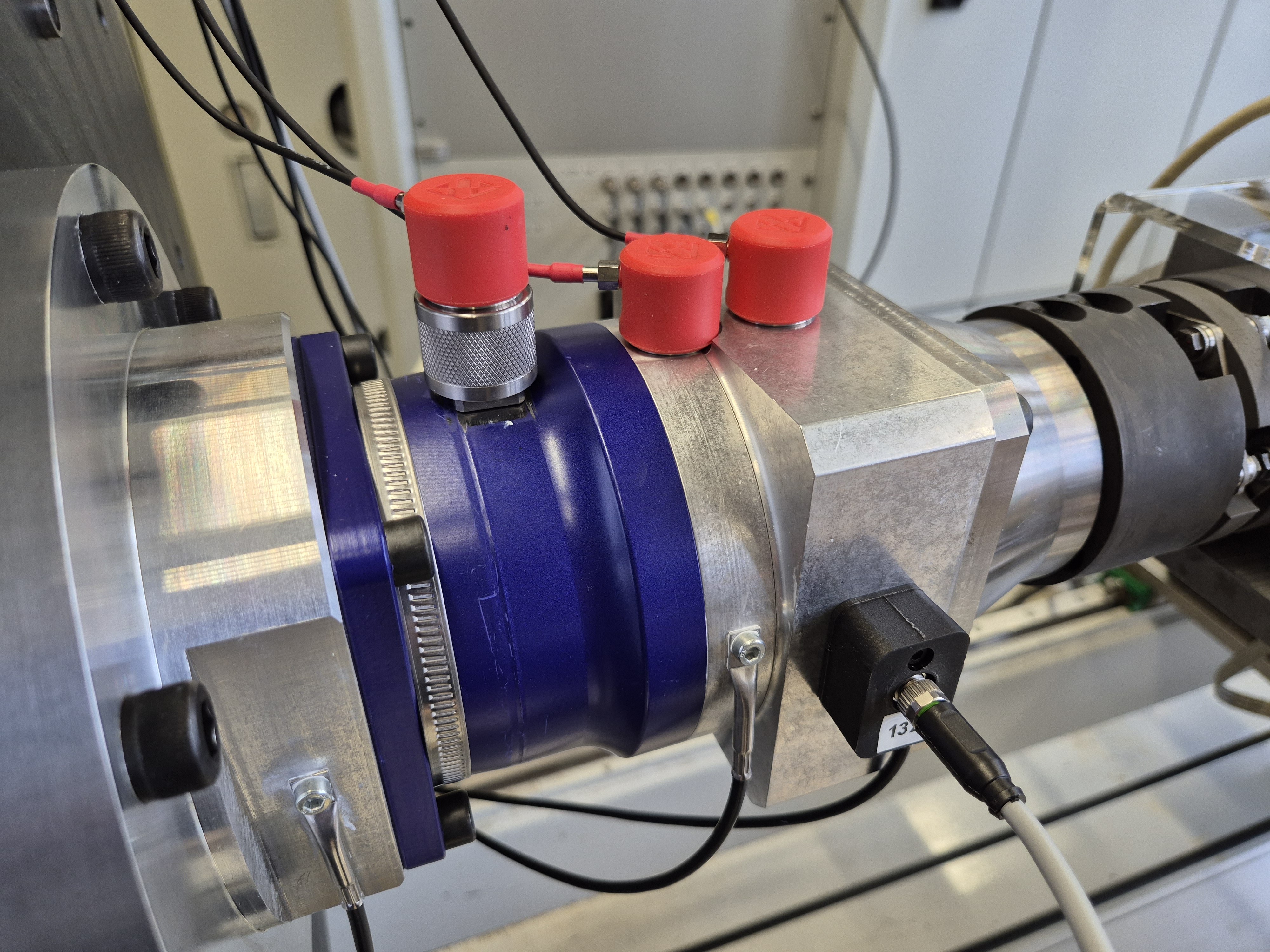 Nahaufnahme eines Planetengetriebes auf dem Prüfstand. Auf der Oberseite sind 3 rote Vibrationssensoren angebracht, auf der Vorderseite des Getriebes 3 Temperatursensoren.