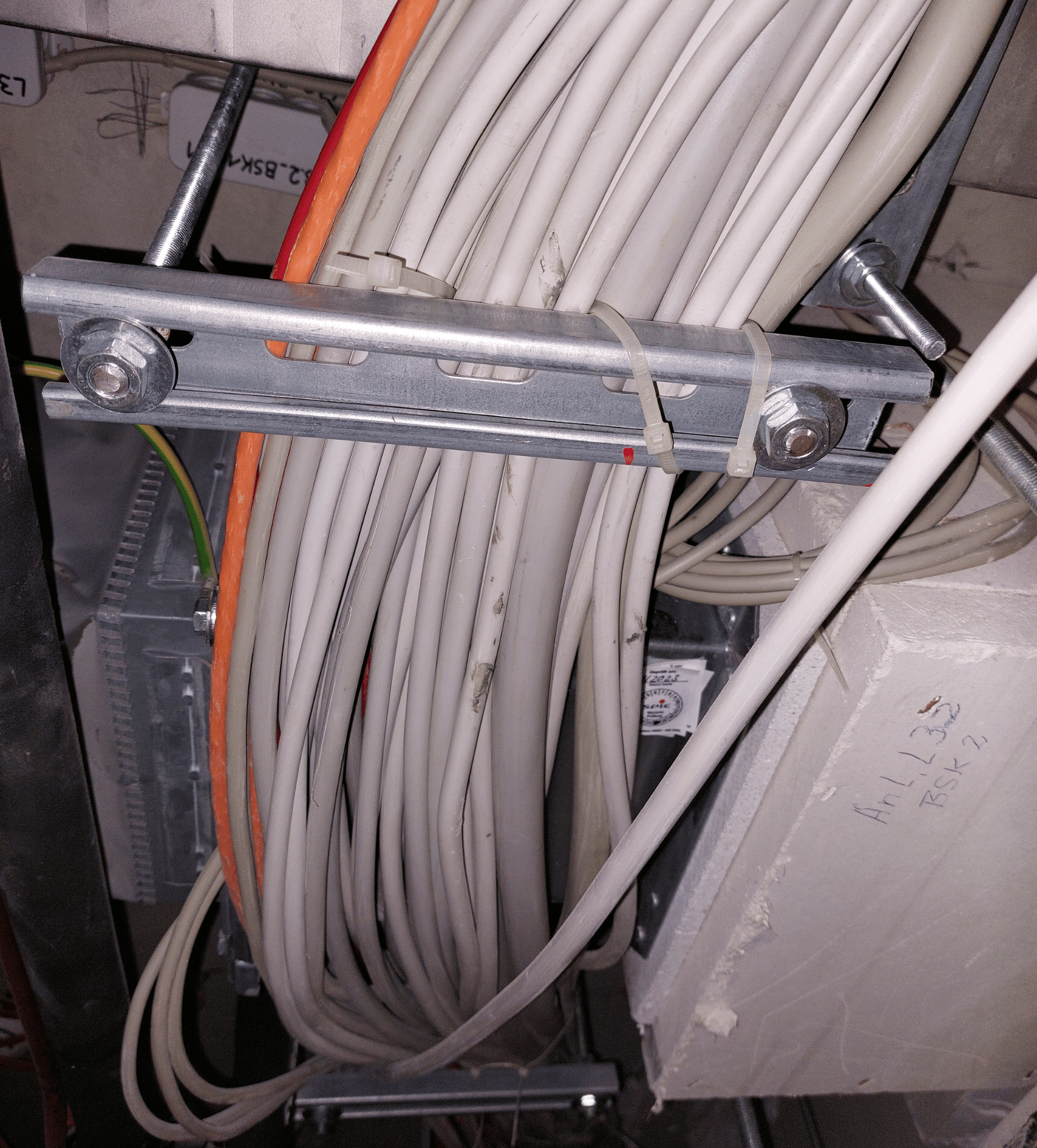 Eine Brandschutzklappe, die in einer L90-Leitung entfernt von der Wand angeordnet ist. Die Klappe lässt sich nur erahnen, da unterhalb der Klappe mehrere elektrische Kabel über Traversen verlegt sind. Die Klappe ist deshalb nicht
