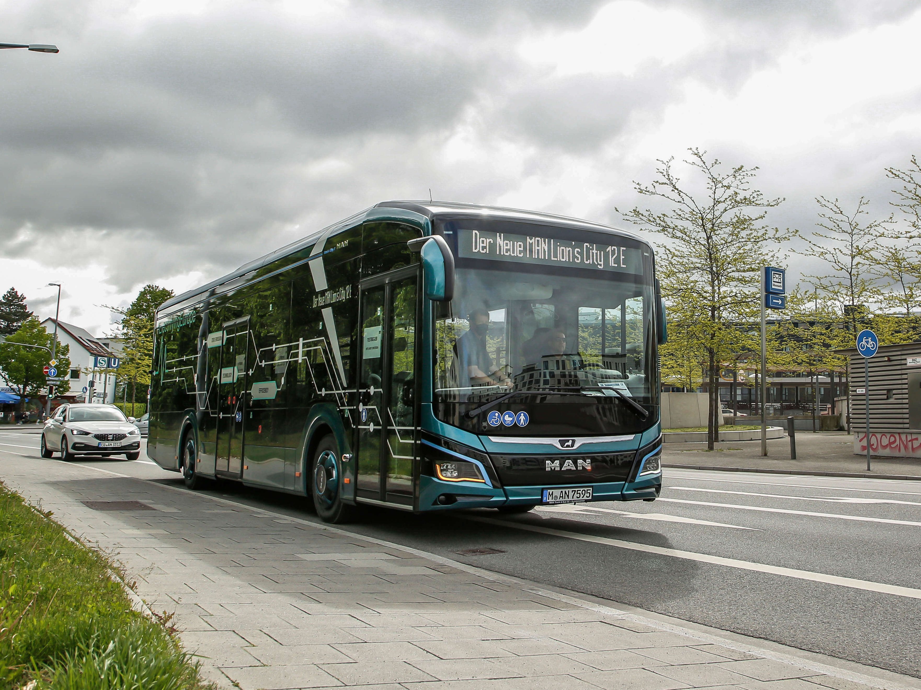 Moderner MAN-Elektrobus Lion’s City 12 E fährt durch eine Stadt, im Hintergrund Autos und Haltestelle.