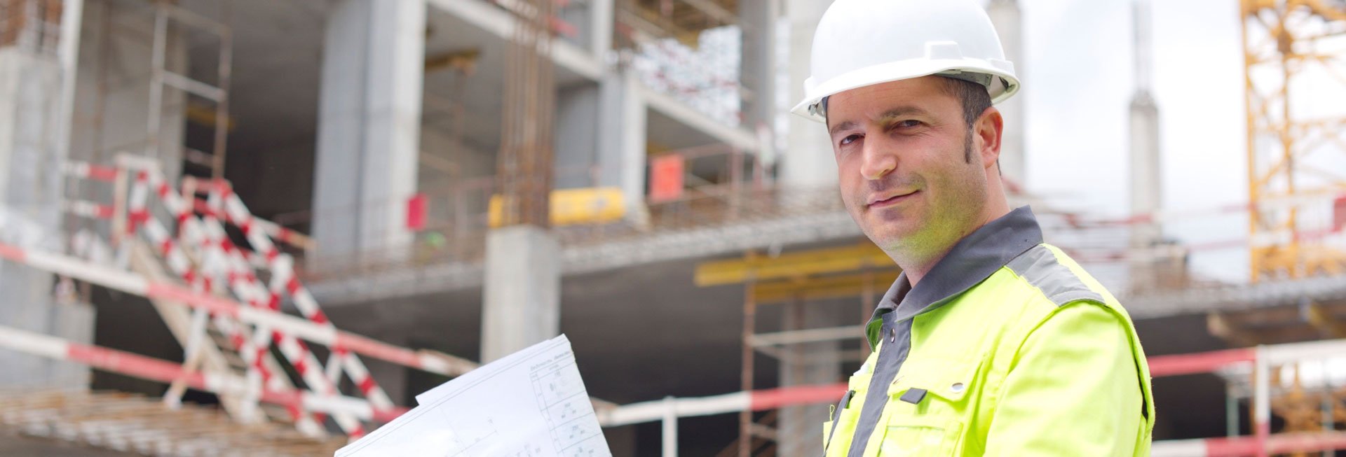 Mann steht mit einem Bauplan in der Hand auf einer Baustelle.